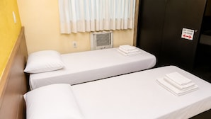 Habitación de hotel con dos camas individuales, cada una con colchón y almohada blancos, y una mesita con toallas dobladas.