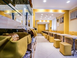 Un restaurante con paredes amarillas, luces de techo blancas y una larga barra con taburetes amarillos.
