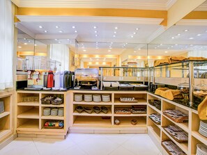 A well-lit breakfast area with a coffee machine, buffet counter, and neatly arranged shelves with plates and baskets.