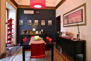 Un comedor con una mesa negra, sillas rojas y una lámpara colgante roja. Se observan cuadros en la pared y una consola negra con objetos decorativos.