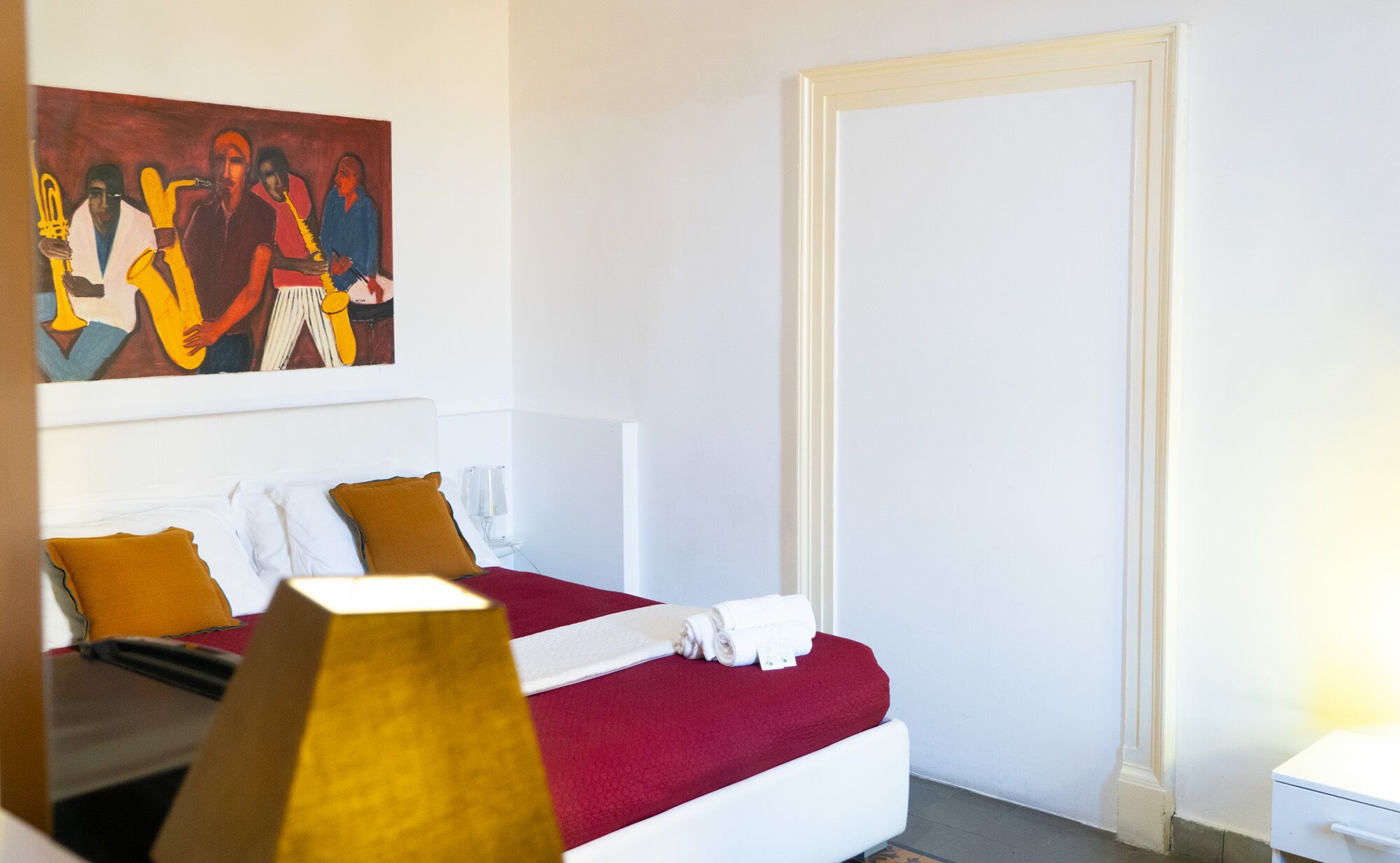 A hotel room with a bed, a painting, a white door, and a nightstand.