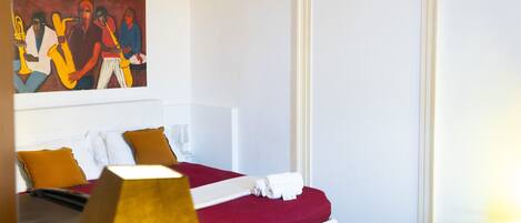 A hotel room with a bed, a painting, a white door, and a nightstand.