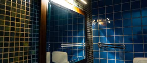 Un baño con paredes de azulejos azules, un espejo, un secamanos y un dispensador de papel higiénico.