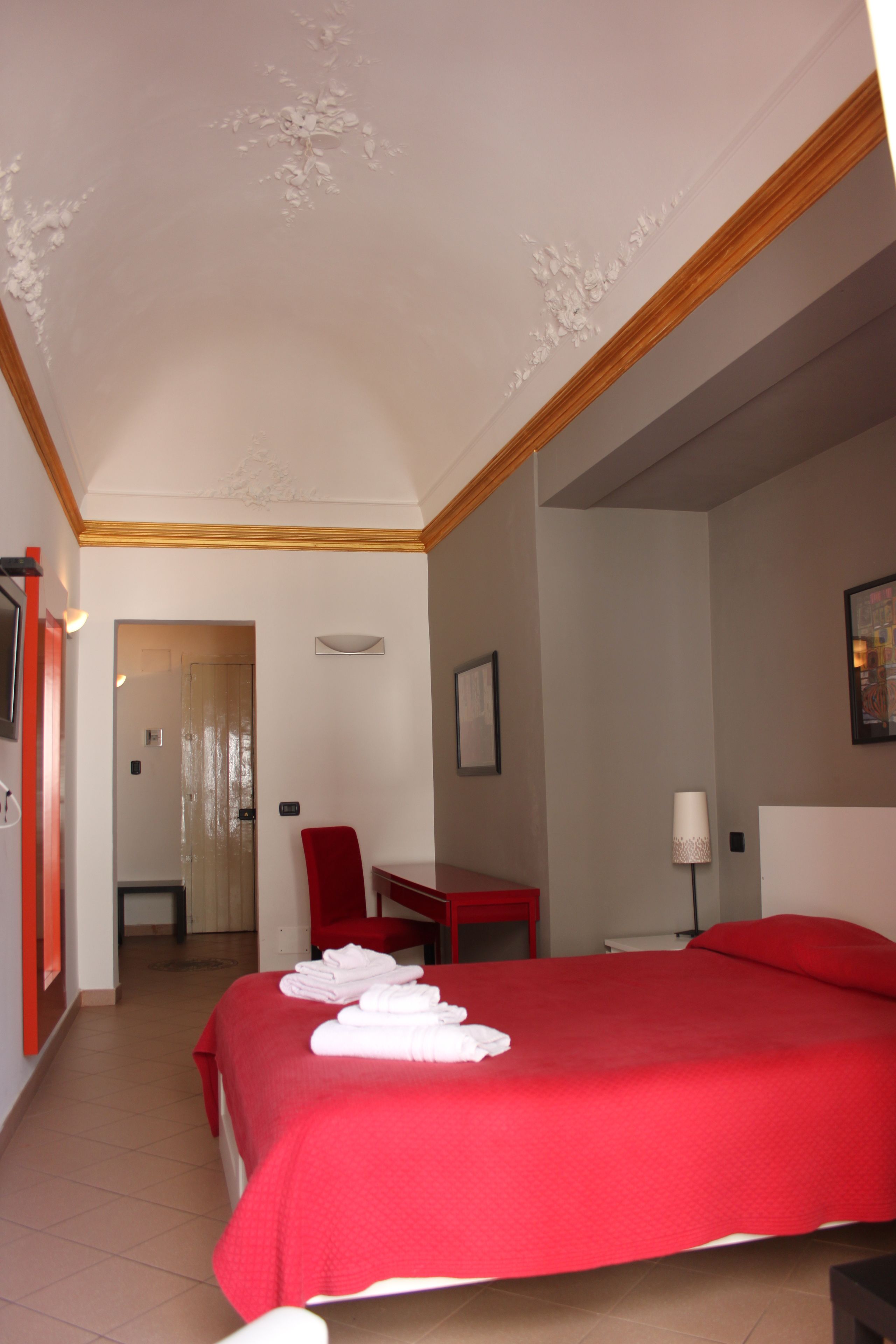 A hotel room with a red bed, a desk, a chair, and a bathroom visible through an open door.