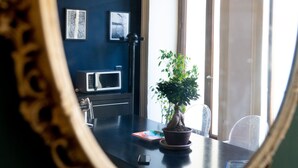Una habitación con pared azul oscuro, una lámpara colgante roja, una planta en maceta, un microondas y un espejo enmarcado.