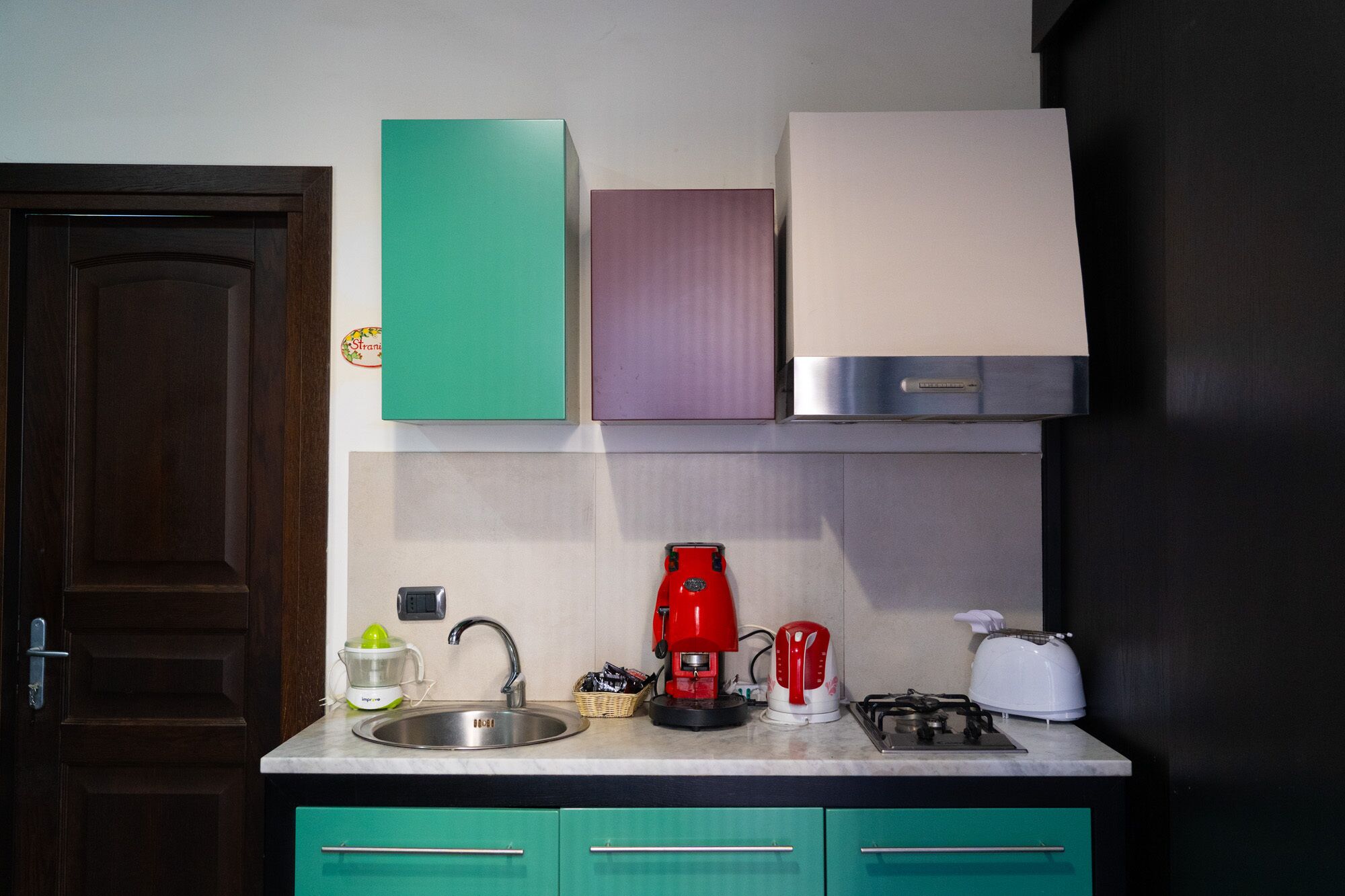 A kitchen with a sink, a coffee maker, a toaster, and green cabinets.
