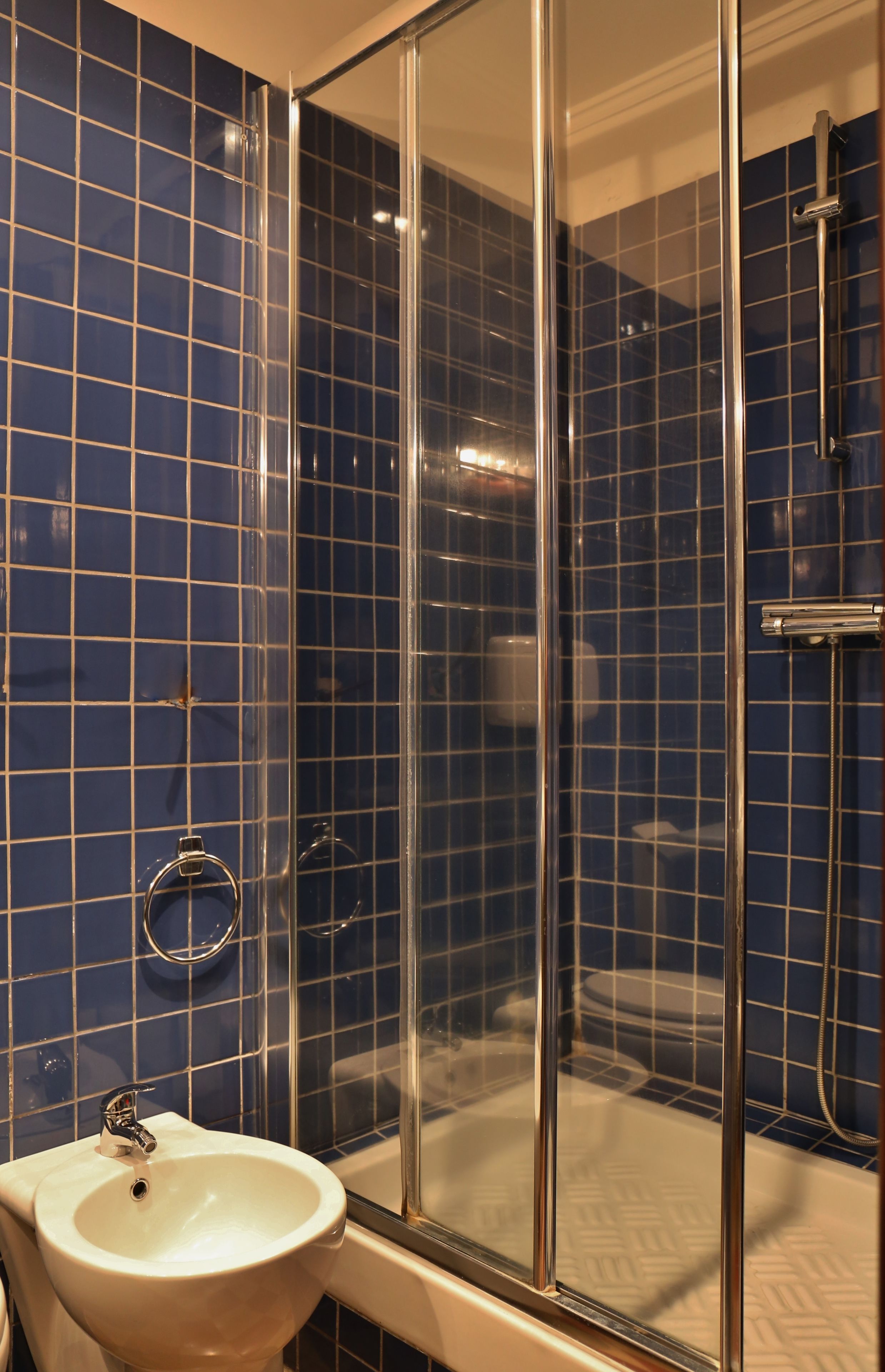 A bathroom with a glass-enclosed shower, a white sink, and blue-tiled walls.