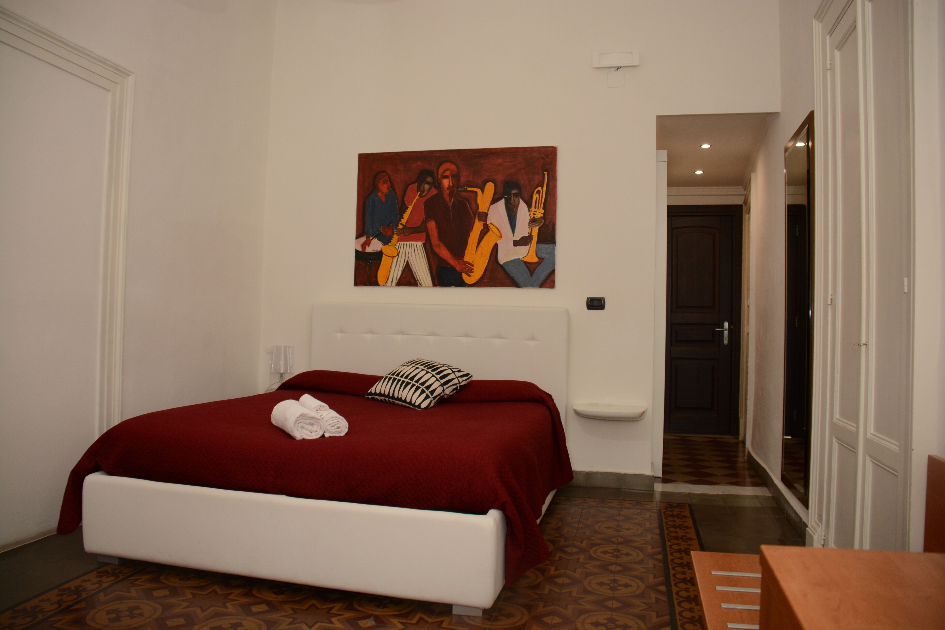 A hotel room with a bed, a painting on the wall, and a bathroom visible through an open door.