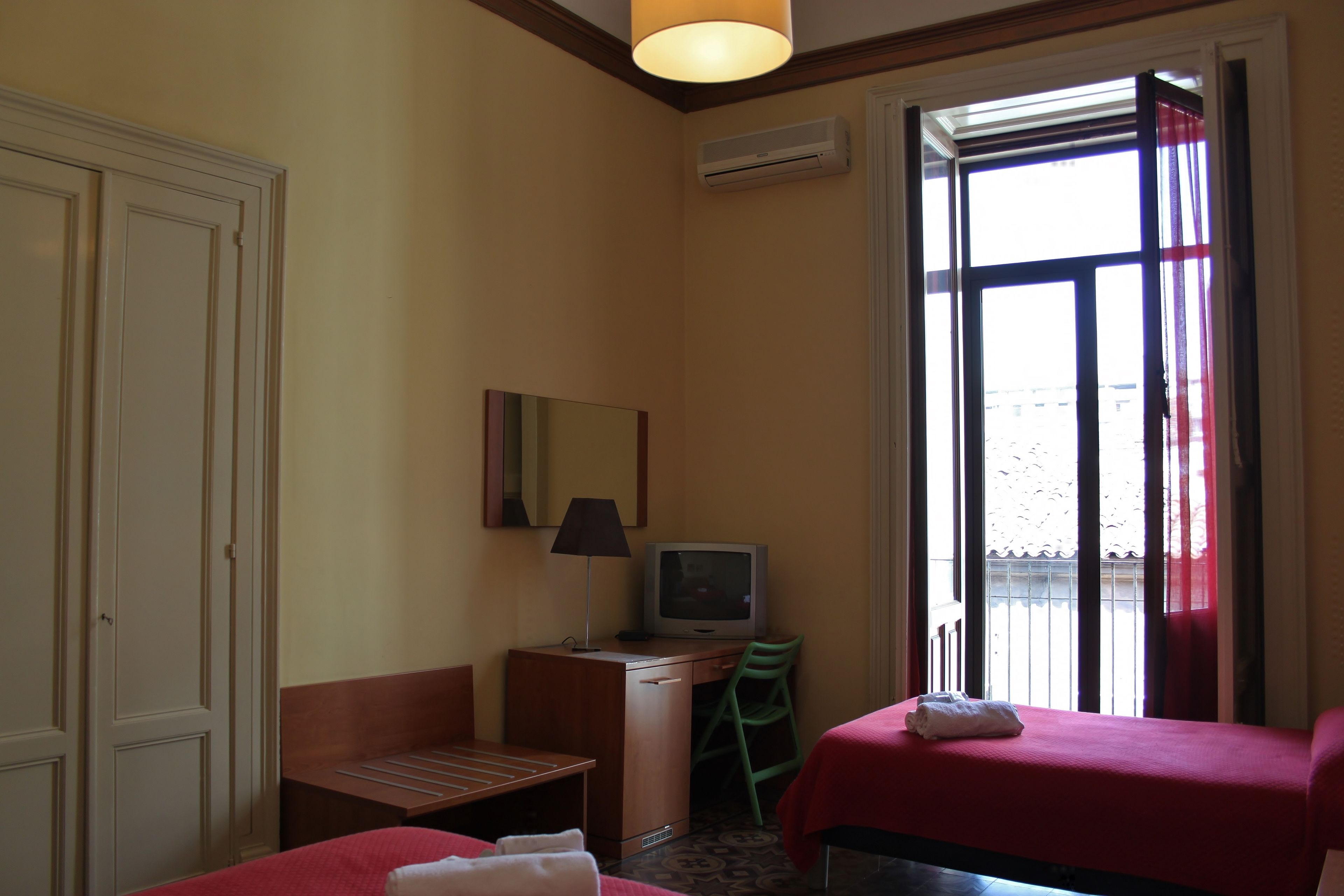Habitación de hotel con dos camas, un escritorio con televisor, una silla, una ventana con cortinas y un equipo de aire acondicionado.