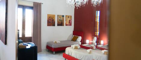 Una camera d'albergo con due letti, un lampadario, opere d'arte alle pareti e una parete di colore rosso.
