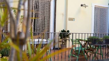 Ein Balkon mit Metallgeländer, grünen Stühlen, einem Tisch und einem Blumentopf.