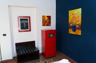 A room with a bench, a red refrigerator, and three framed artworks on the wall.