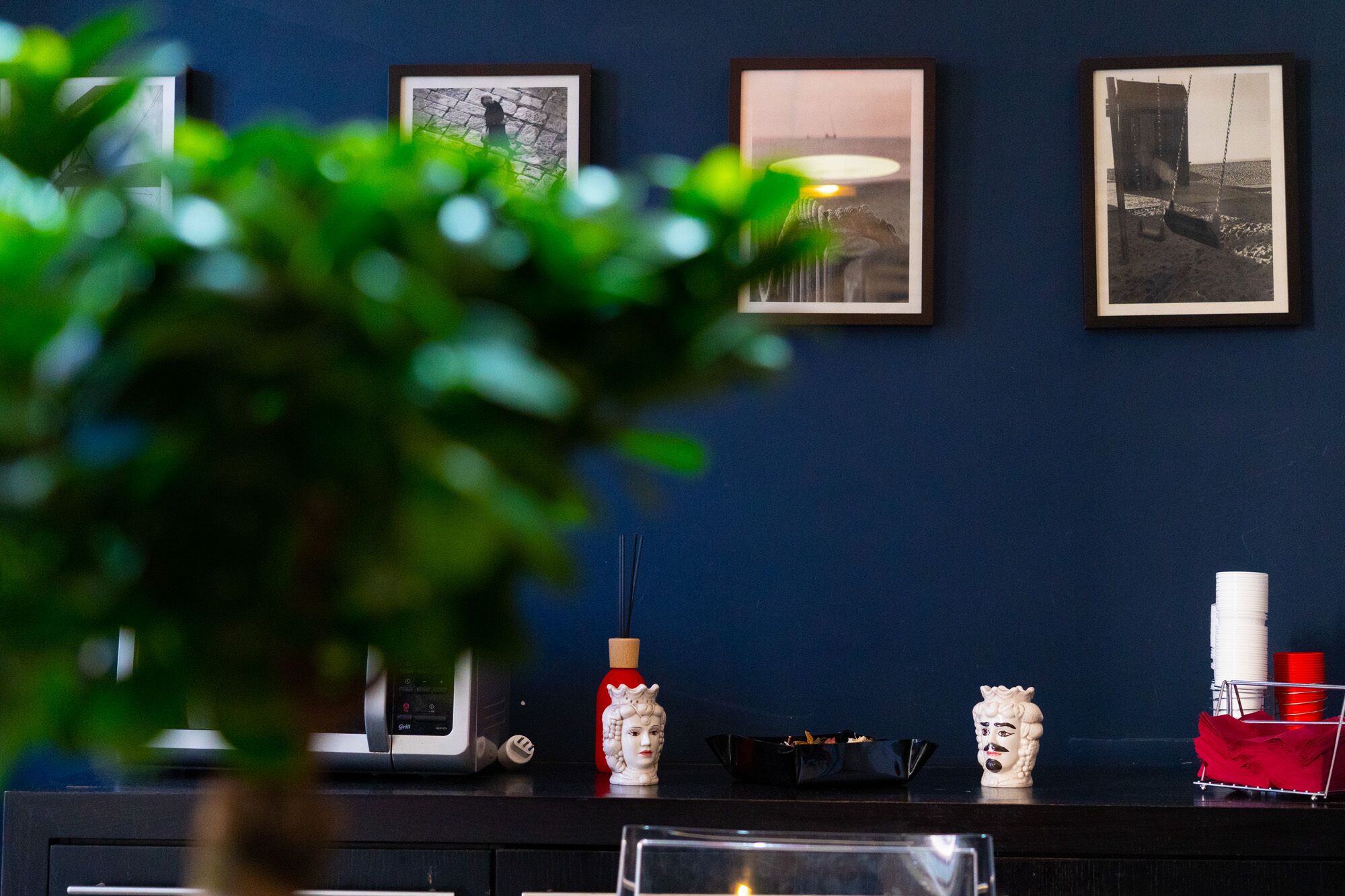A reception desk with framed photographs on the wall, a potted plant in the foreground, and various decorative items including a vase and figurines.
