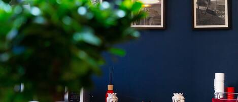 A reception desk with framed photographs on the wall, a potted plant in the foreground, and various decorative items including a vase and figurines.