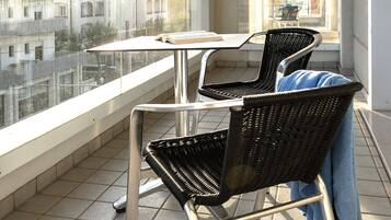 A balcony with two wicker chairs, a small table, and a view of buildings in the background.
