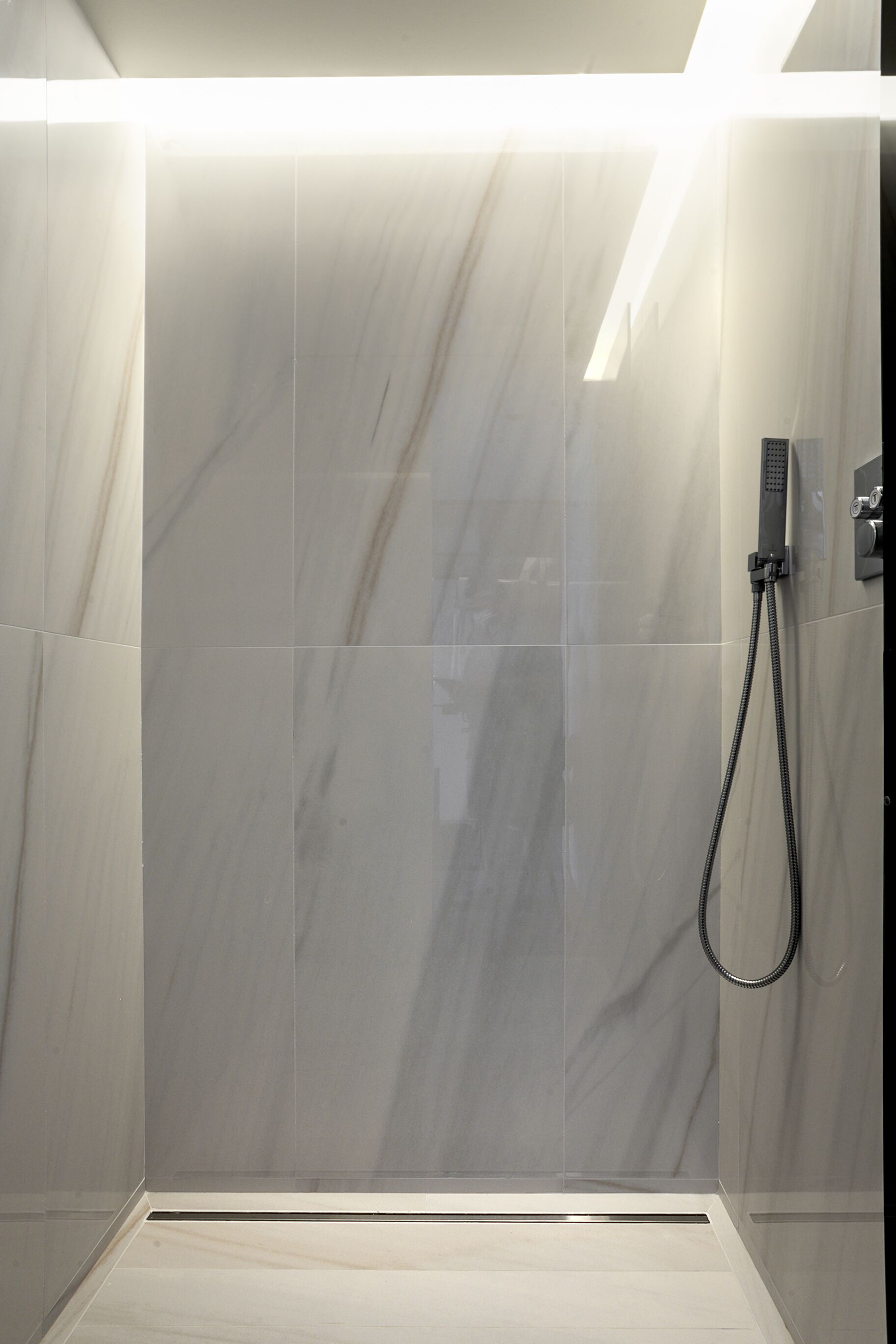 A modern shower with a handheld showerhead, a control panel, and a tiled floor.
