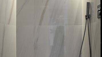 A modern shower with a handheld showerhead, a control panel, and a tiled floor.