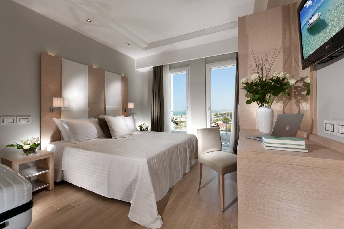 Habitación de hotel moderna con una cama grande, un escritorio con una computadora portátil, un televisor y vista al océano.