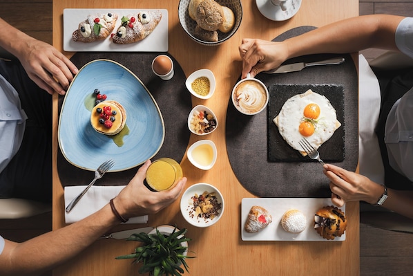 Una mesa de comedor con diversos alimentos para el desayuno, como tortitas, huevos y bollería.
