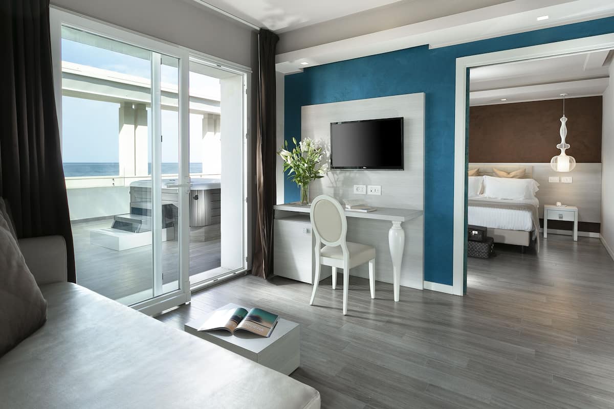 Una habitación de hotel moderna con balcón, escritorio, televisor, cama y vista al océano.