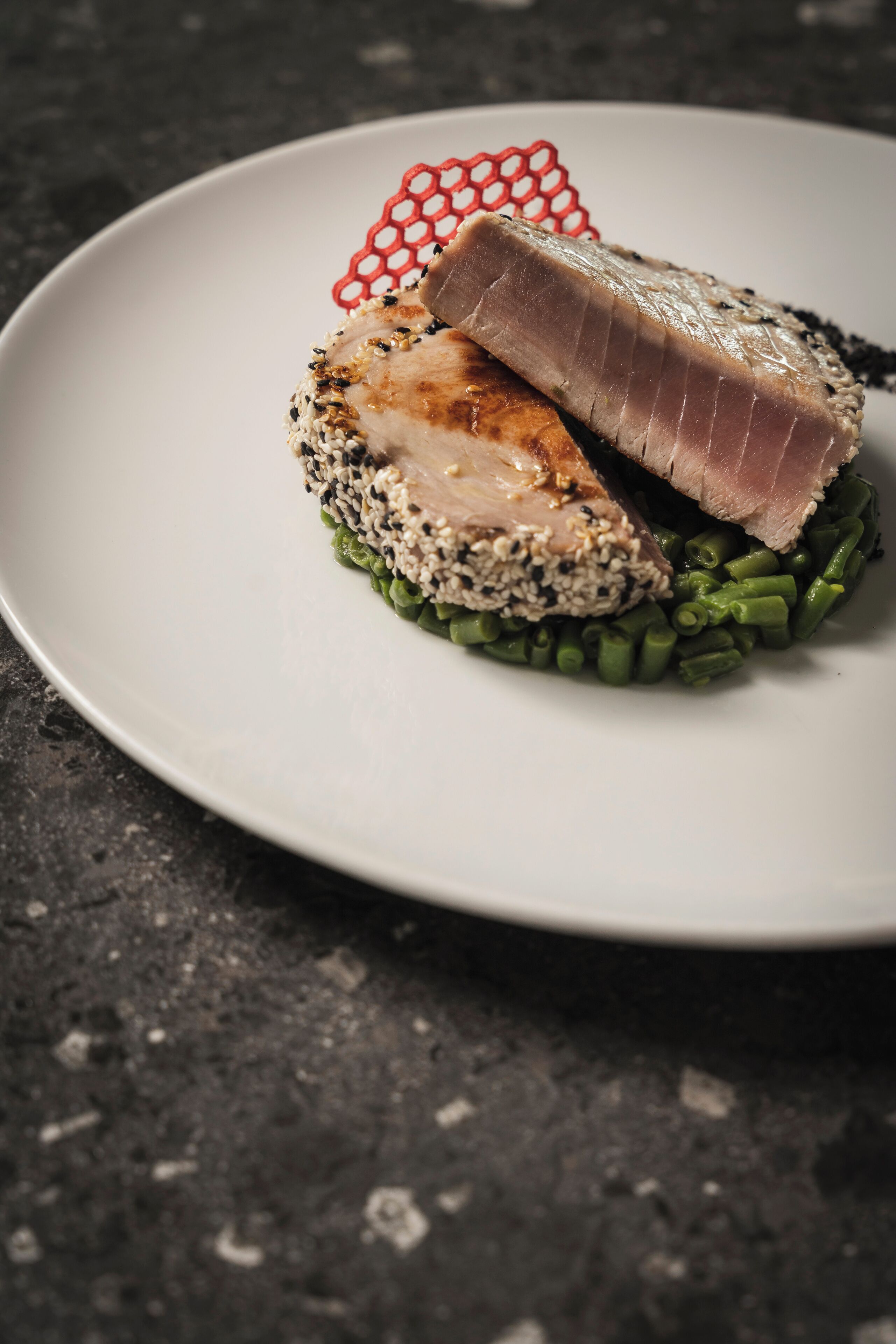 A plate with a piece of meat, green beans, and a decorative red element.