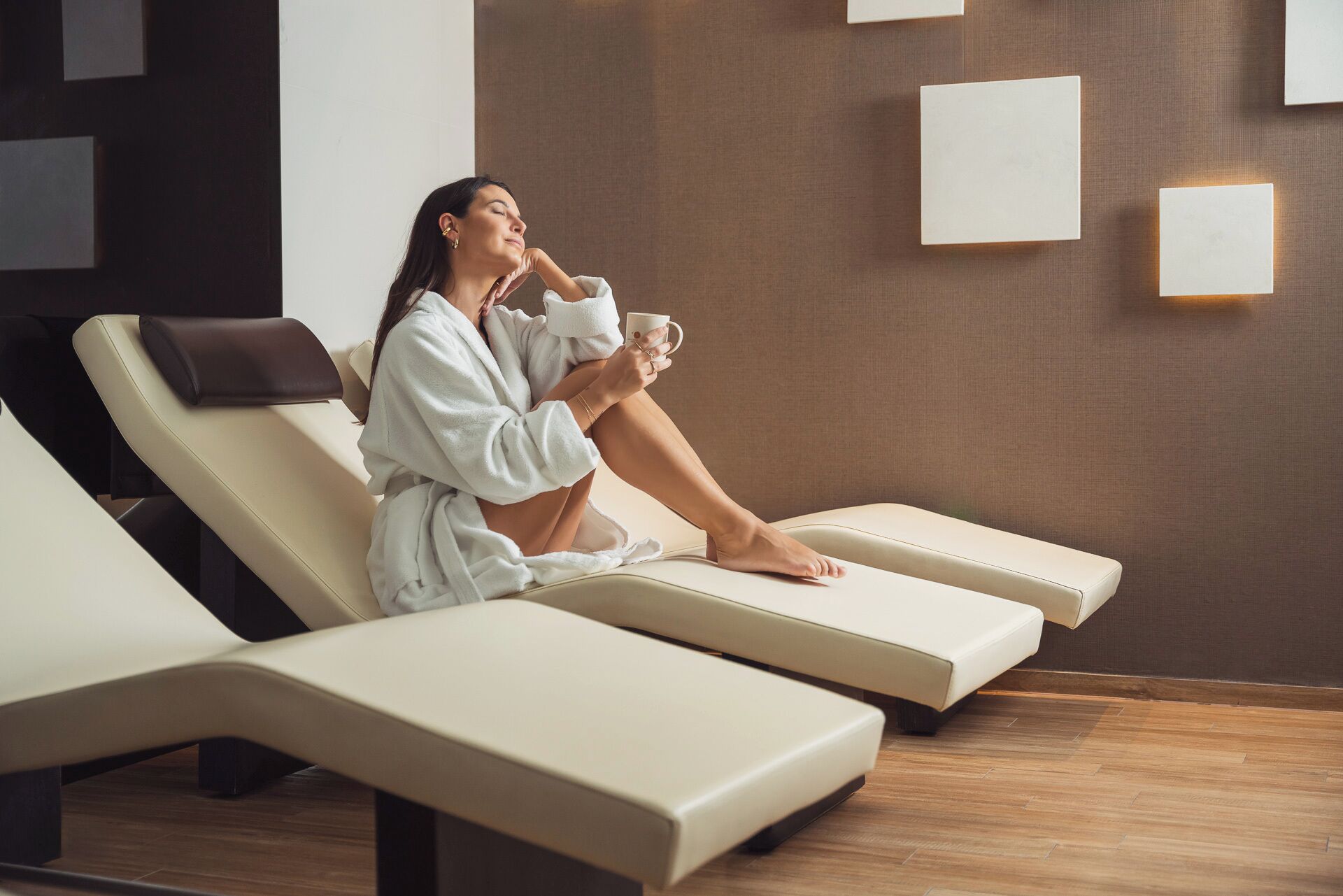 A person relaxing on a sun lounger in a spa-like setting with a wall-mounted light fixture.