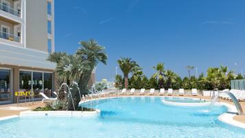 A swimming pool with lounge chairs, palm trees, and a building with balconies.