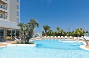 Una piscina con lettini, palme e un edificio con balconi.