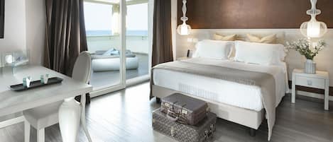 A modern hotel room with a large bed, a desk, and a view of the sea.