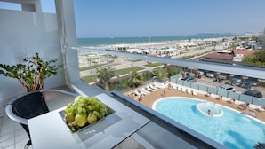 Un balcón con piscina, un área de comedor con frutero y vistas a la playa y al horizonte urbano.