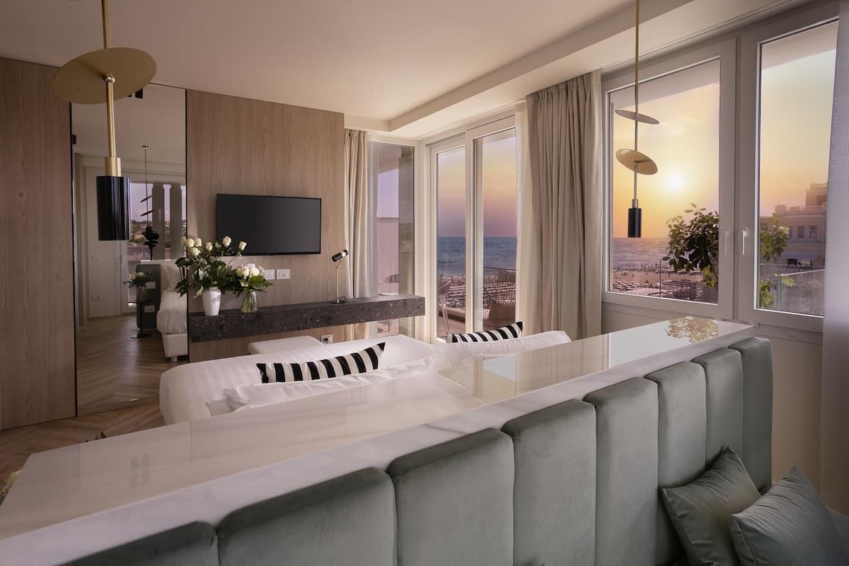Habitación de hotel moderna con un amplio ventanal que ofrece vistas a la ciudad, una zona de estar cómoda, un televisor de pantalla plana y una decoración minimalista.