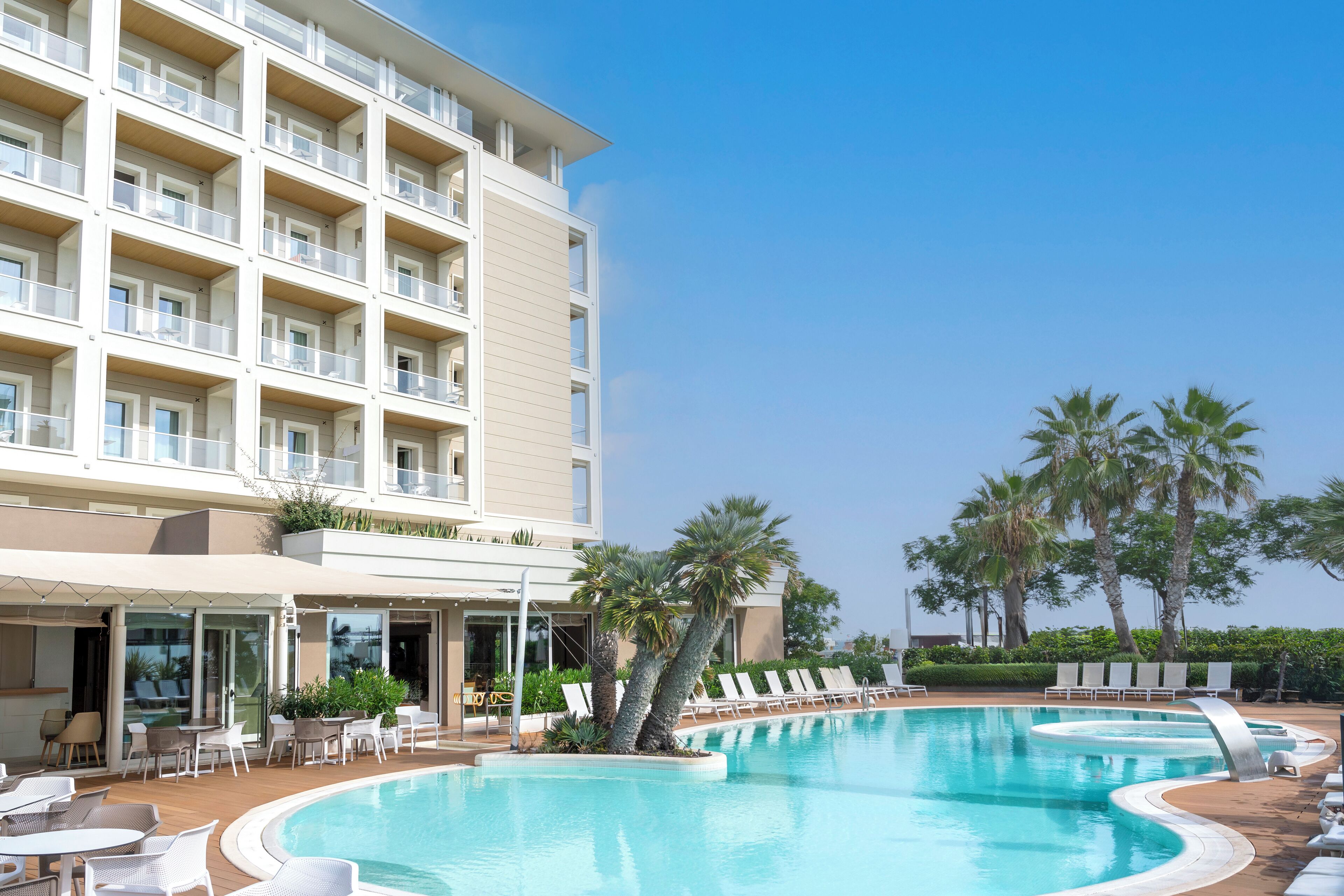 Un hotel con piscina, mobiliario exterior y palmeras.