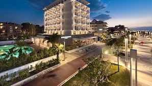 Un hotel moderno con varios pisos, piscina y un área exterior bien iluminada.