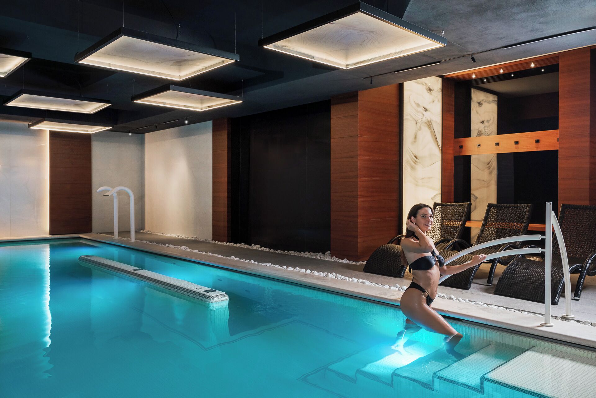 A swimming pool with a person in the water, lounge chairs, and a modern interior design.