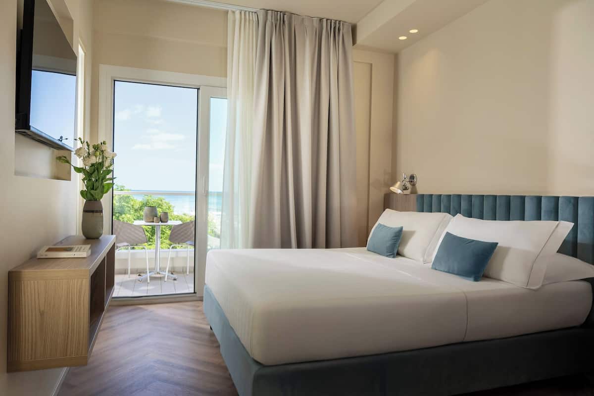 Habitación de hotel con una cama grande, un escritorio y vista al mar.