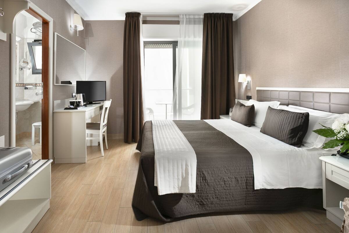 Habitación de hotel con cama, escritorio con televisión, baño y vista al exterior.