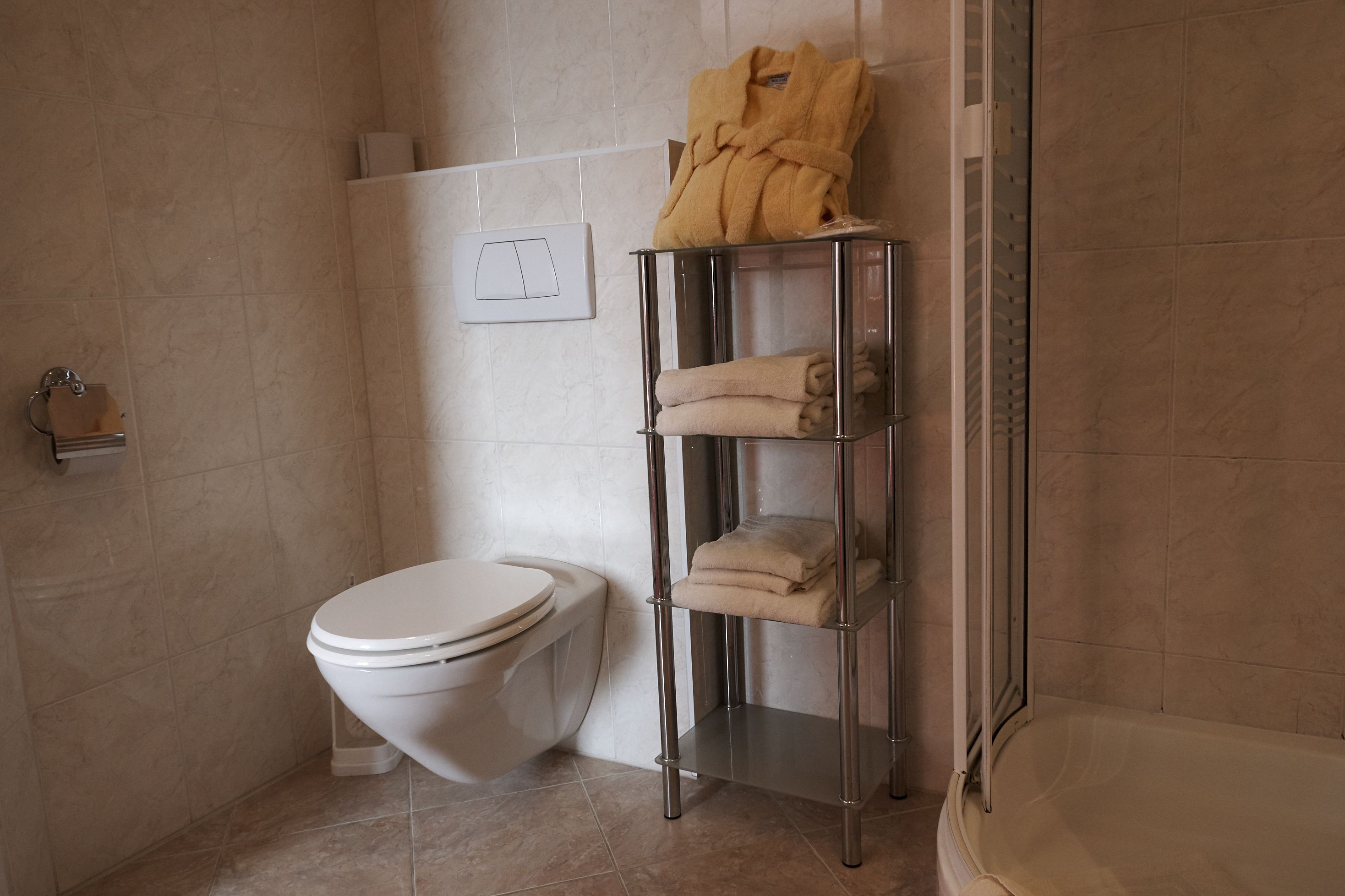 A bathroom with a toilet, a towel rack with folded towels, and a shower area.