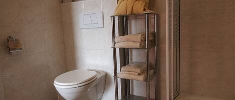 A bathroom with a toilet, a towel rack with folded towels, and a shower area.