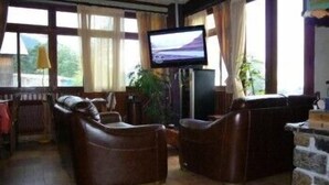 Una sala de estar acogedora con sofás de cuero, un televisor de pantalla plana y ventanas grandes con cortinas.