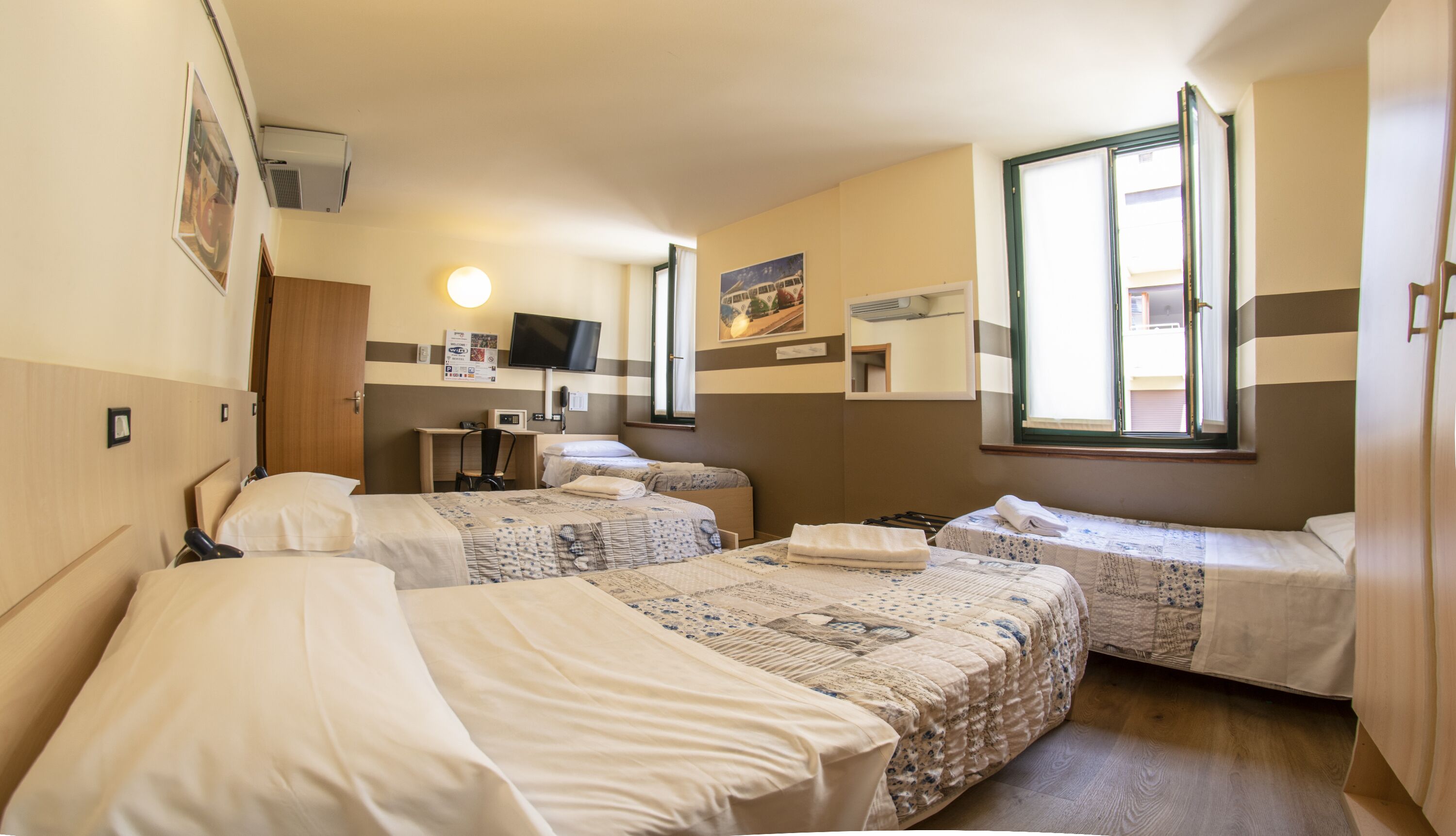 Habitación de hotel con dos camas individuales, un escritorio, una silla, un televisor de pantalla plana y un ventanal con vistas al exterior.