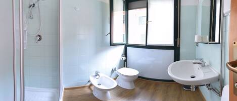 A bathroom with a shower, two toilets, a sink, and a window.