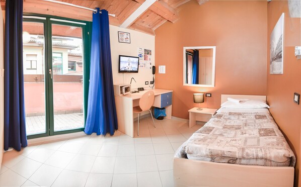 A hotel room with a bed, desk, chair, and a sliding glass door to the outside. - Central Hostel BG (Bergamo)