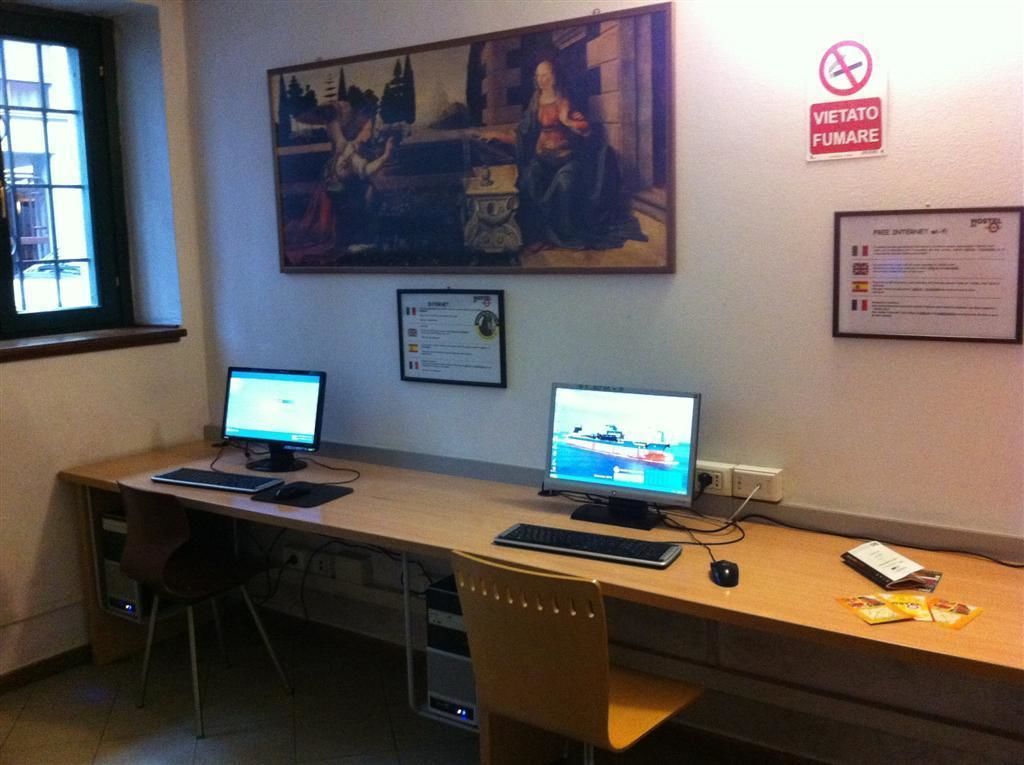 Una habitación con dos escritorios, cada uno con un monitor de computadora, teclado y ratón. Hay un cuadro en la pared y un cartel que indica prohibido fumar.