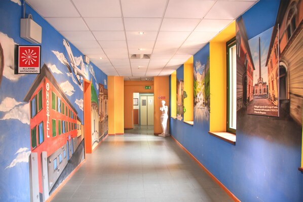 Un pasillo de hotel con paredes azules y amarillas, un mural rojo en la pared del edificio y una estatua.