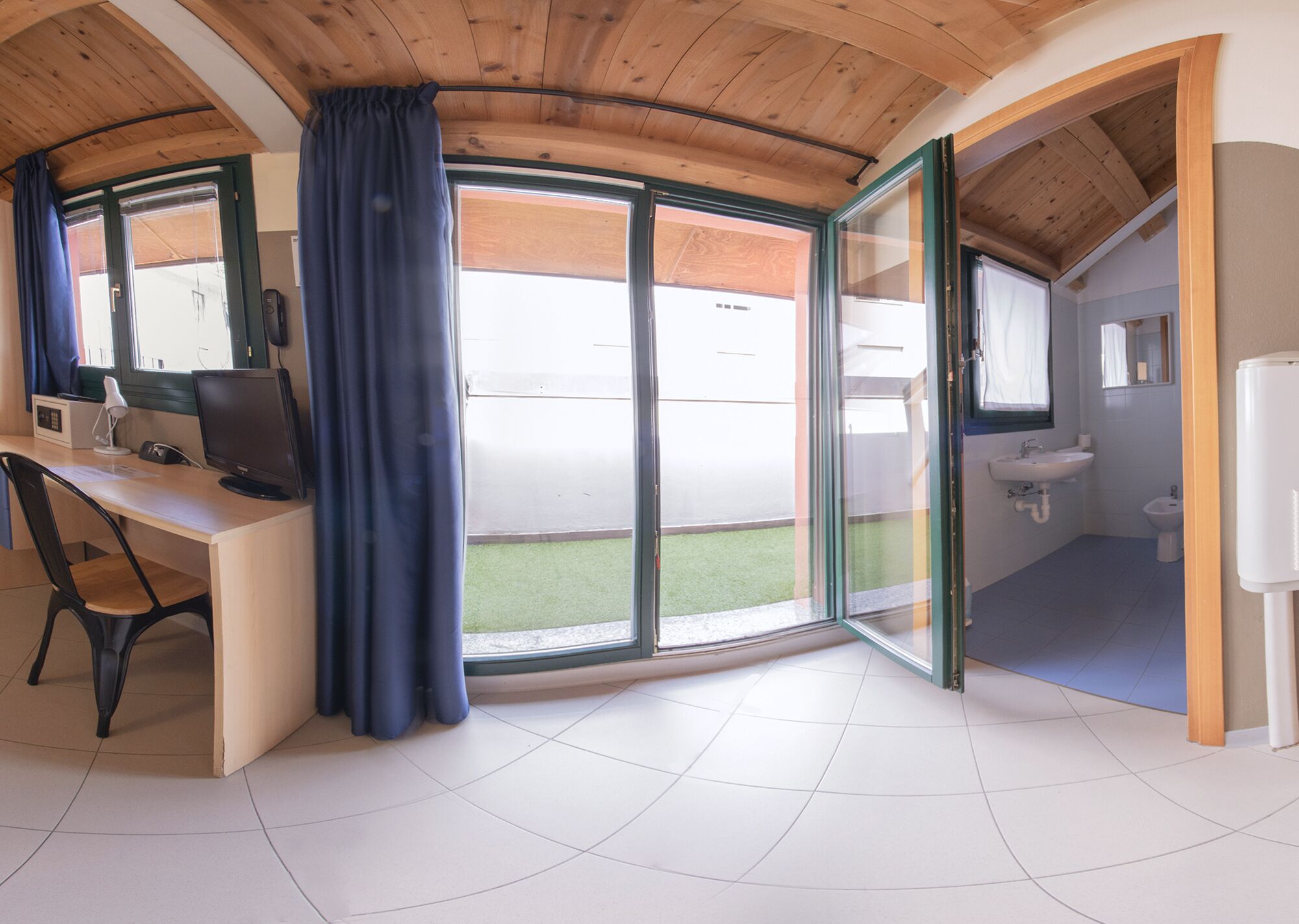 Habitación con escritorio, computadora y vista a un jardín verde a través de amplios ventanales correderos.