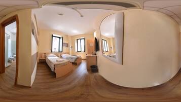 A panoramic view of a hotel room with a wooden floor, two beds, a desk, and a window.