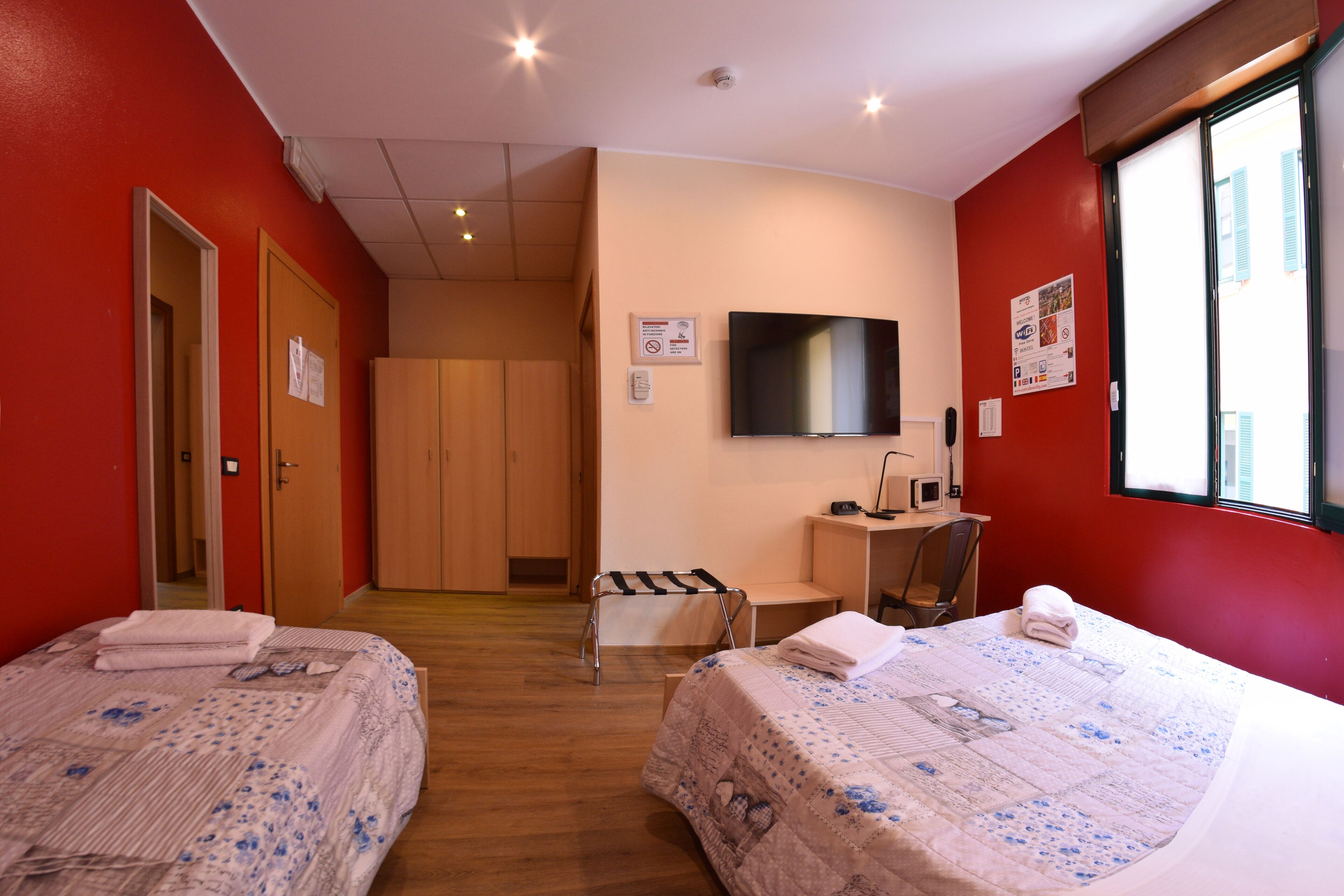 A hotel room with two beds, a TV, a desk, and a window.
