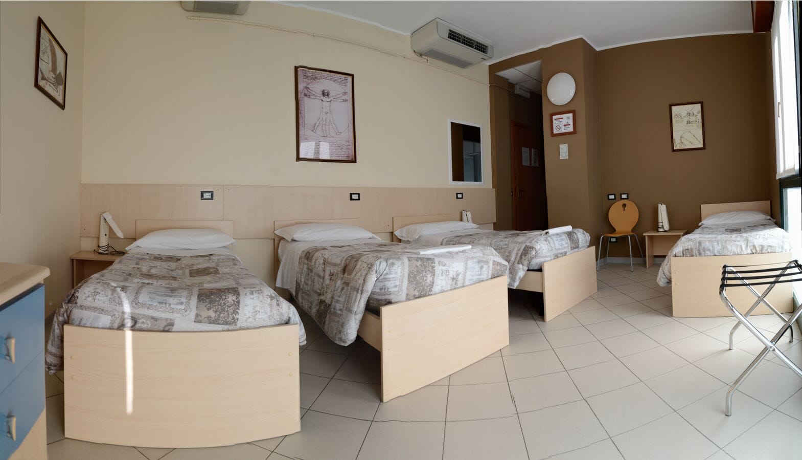 Ein Hotelzimmer mit drei Betten, einem Schreibtisch, einem Stuhl und einem Fenster.