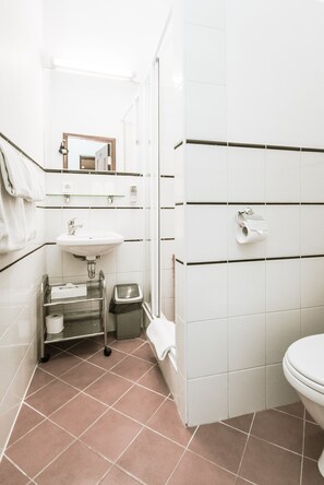 Un baño con azulejos blancos, un lavamanos, un inodoro y un espejo.