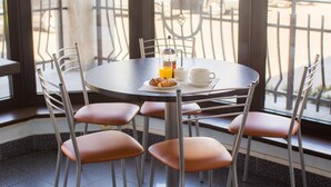 A round table with breakfast items, including croissants, orange juice, and coffee, surrounded by chairs. - Kert (Riga)